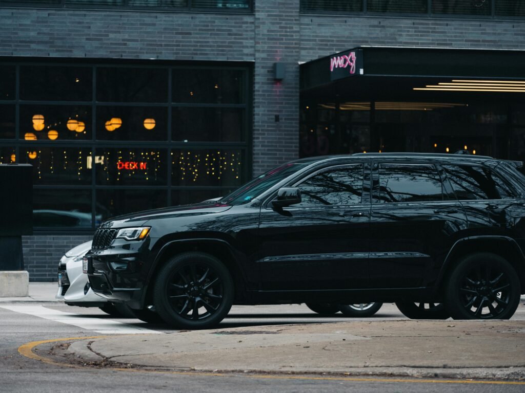 A sleek black SUV parked on a city street with modern buildings and outdoor lighting.